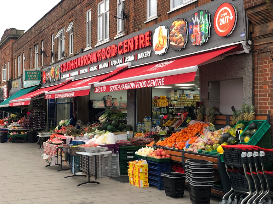 The exterior of South Harrow Food Centre, a grocery shop located on a street with red brick buildings. The shop features a large red and white sign with the store's name and categories including Asian